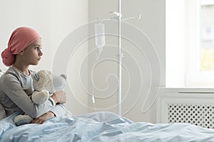 Sick girl wearing headscarf and hugging plush toy in the hospital