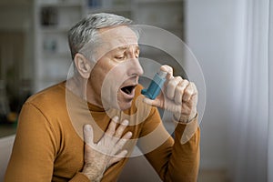 Sick grey-haired senior man touching chest and using asthma inhaler