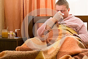 Sick guy in a pink bathrobe, lying in the bed and blowing