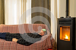 Sick Hispanic man lying on the couch with a robe and a cloth on his forehead in the heat of a pellet stove.