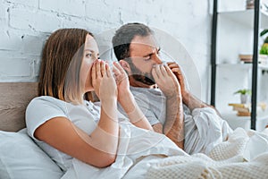 sick husband and wife sneezing while