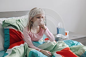 Sick ill kid girl with fever lying in bed at home with flu, fever, running nose and coughing in hand fist. Virus cold season flu