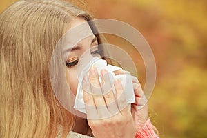 Sick ill woman in autumn park sneezing in tissue.