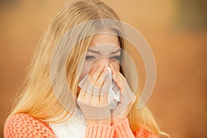 Sick ill woman in autumn park sneezing in tissue.