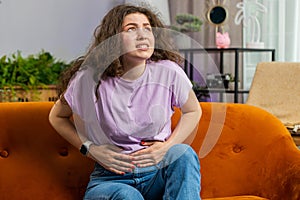 Sick ill woman suffering from period cramps, stomach ache menstrual pain lying on sofa at home room