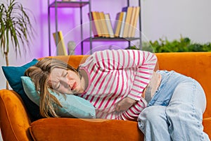 Sick ill woman suffering from period cramps, stomach ache menstrual pain lying on sofa at home room