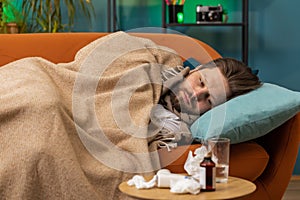 Sick ill young man suffering from cold or allergy lying on home sofa sneezes wipes snot into napkin