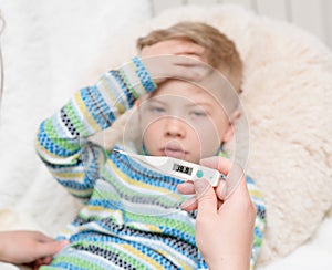 Sick kid with high fever laying in bed and mother checks the temperature