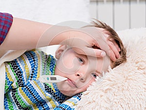 Sick kid with high fever laying in bed and mother taking tempera