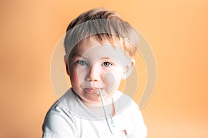 Sick kid with a thermometer in his mouth with sad face on orange background