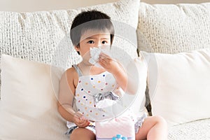 Sick little Asian girl wiping or cleaning nose with tissu