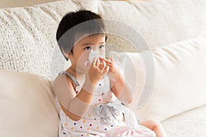 Sick little Asian girl wiping or cleaning nose with tissue