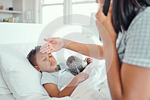 Sick little boy in bed while his mother talks on the phone calling doctor for help to bring fever down. Young single