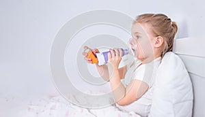 Sick little girl with asthma medicine lying in bed. Unwell kid with chamber inhaler for cough treatment. Flu season. Bedroom or