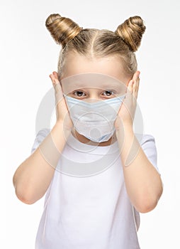 A sick little girl with blond hair in a medical mask is holding her head with her hands. Medical concept of epidemiological period