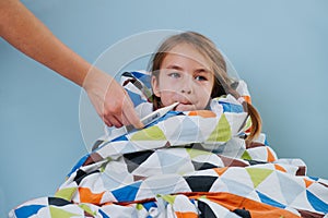 Sick little girl with common cold sitting in bed under blanket with thermometer