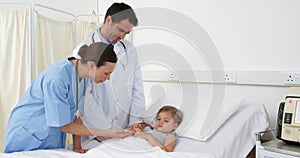 Sick little girl lying in bed talking to nurse and doctor