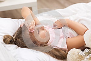 Sick little girl lying in bed with thermometer