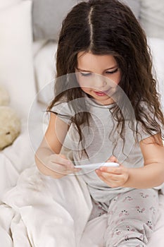 Sick little girl lying in bed with thermometer