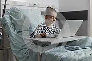 Sick little girl playing games on laptop while hospitalized