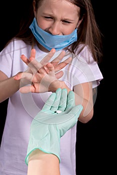 Sick little girl refuses to take a pill from a doctor. On the girl`s face there is a mask to protect against Covid-19