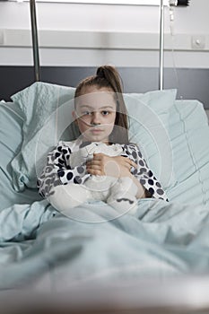 Sick little girl under treatment wearing oxygen tube while holding plush bear toy.
