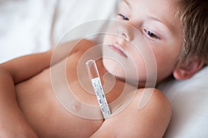 Sick little kid lying with a thermometer with high temperature in the armpit