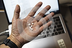 Sick male home office worker taking pills in front of his working space, during his working deadline night.