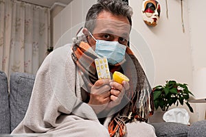 Sick male model wearing medical mask presenting lemon and pills