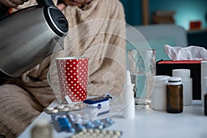 Sick man with Blanket making Tea while sitting on sofa. Ill person feeling bad having medical treatment of influenza