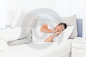 Sick man blowing his nose lying on his bed