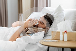 sick man blowing nose lying in bed at home