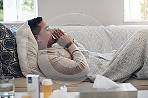 Sick, man and blowing nose with tissue for flu, sinus or illness on living room sofa at home. Tired male person with