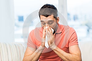 Sick man blowing nose to paper napkin at home