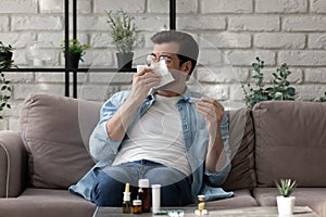 Sick man blowing running nose, holding thermometer, feeling unwell