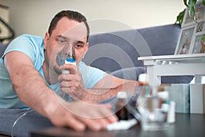 A sick man breathes through an inhaler mask. lying on the couch and pulls his hand to the cure photo