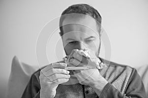 Sick man checks the body temperature with a mercury thermometer. Theme of viral diseases, flu, colds. Monochrome effect