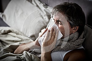 Sick man with cold lying in bed and blow nose. photo