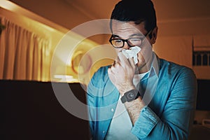 Sick man covering his nose with tissue paper working late on laptop