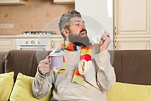 Sick man with flu drinks hot tea at home. Bearded man with cold blow nose