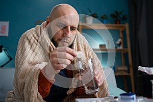 Sick man with headache sitting under the blanket, putting pill in water. Suffering flu, allergy sitting on couch. Man