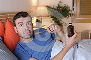 Sick man holding syrup bottle in bed