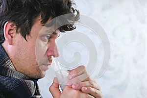 Sick man inhaling through inhaler nozzle for nose. Close-up face, side view. Use nebulizer and inhaler for the treatment