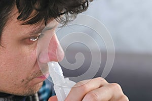 Sick man inhaling through inhaler nozzle for nose. Close-up face, side view. Use nebulizer and inhaler for the treatment