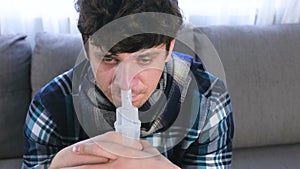 Sick man inhaling through inhaler nozzle for nose sitting on the sofa. Close-up face, front view. Use nebulizer and