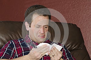 Sick man looking at a tissue after blowing his nose.