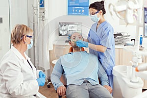 Sick man preparing for tooth surgery while nurse putting medical oxigen mask