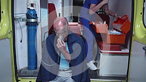 Sick man sit in oxygen mask in ambulance car.