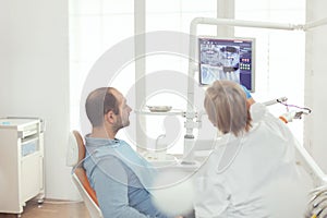Sick man sitting on dental chair looking at teeth radiography