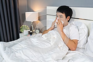 Sick man sneezing into tissue lying in bed